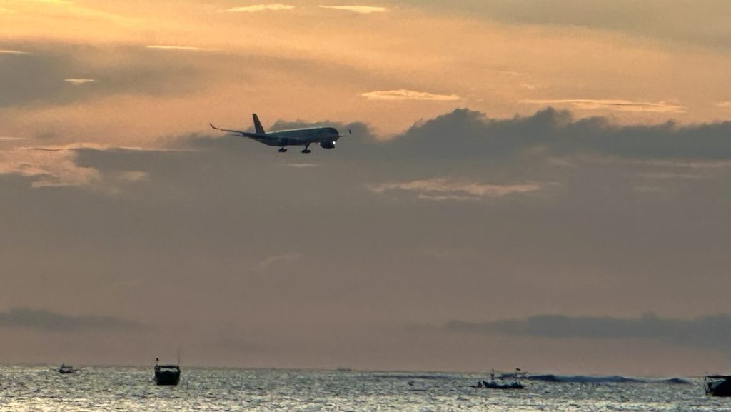 ジンバランビーチの夕景を横切る着陸前の飛行機