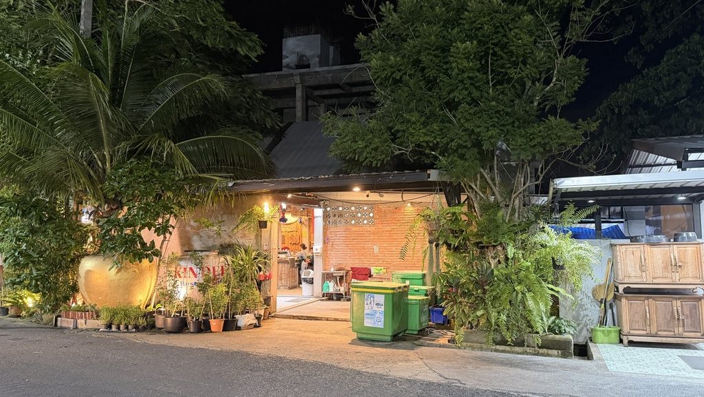 夜の照明に照らされた緑の多いKin Dee Restaurantの入口
